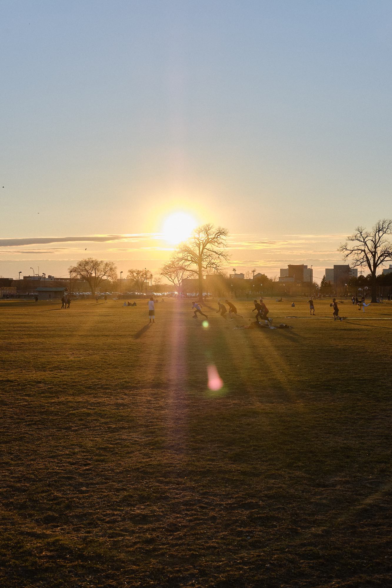 A group of men are playing a team sport—maybe rugby—as the sun sets behind them