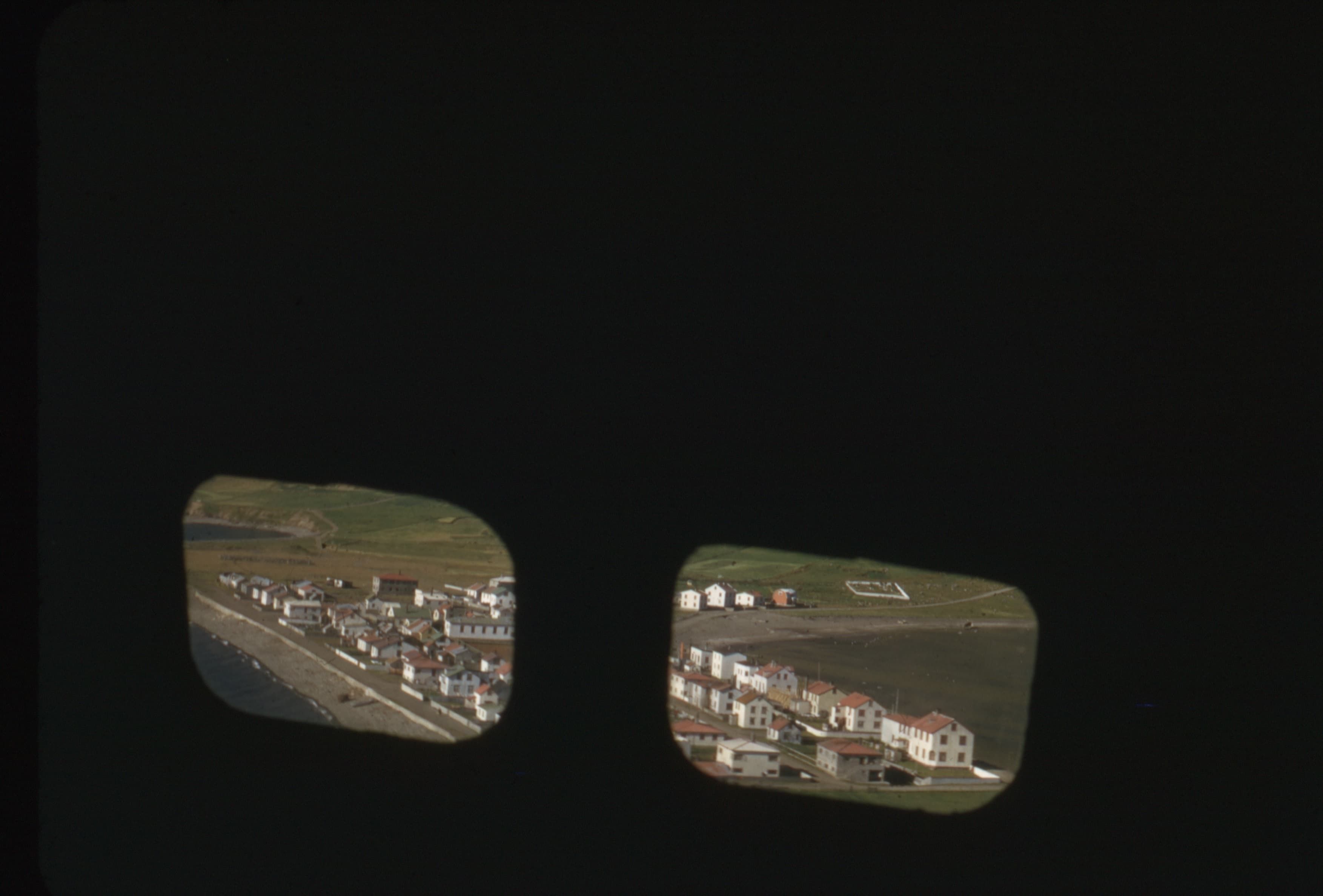 A photo taken from inside a small airplane turning around a small Icelandic fishing village.